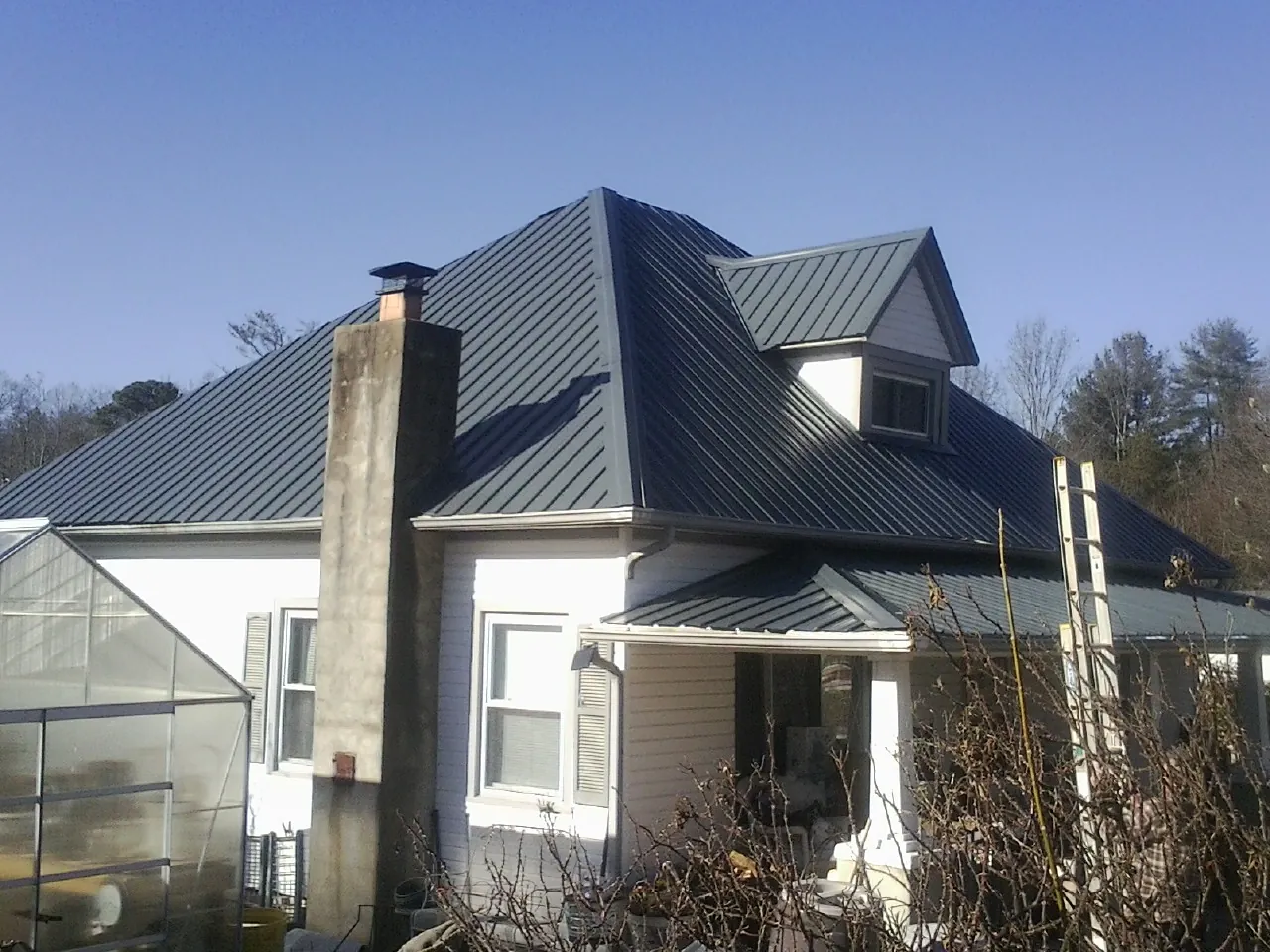 Dark blue standing seam metal roof on a white farmhouse with dormer — Slate & Tile Roof Repair by Roofing Brothers in Mesick