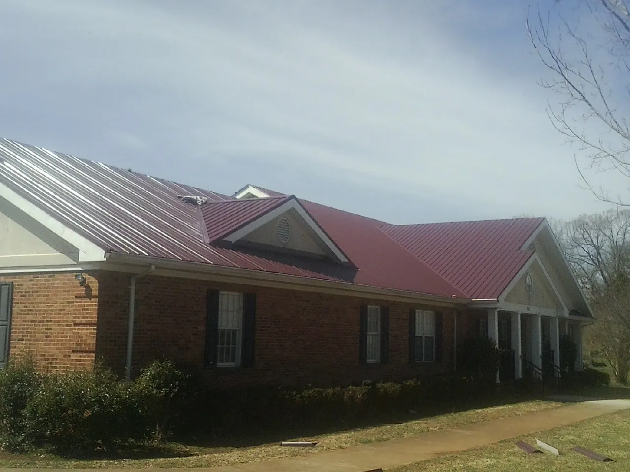 Red metal roof with gabled entries on a long brick building, from a Hail Damage Roof Repair job in Mesick