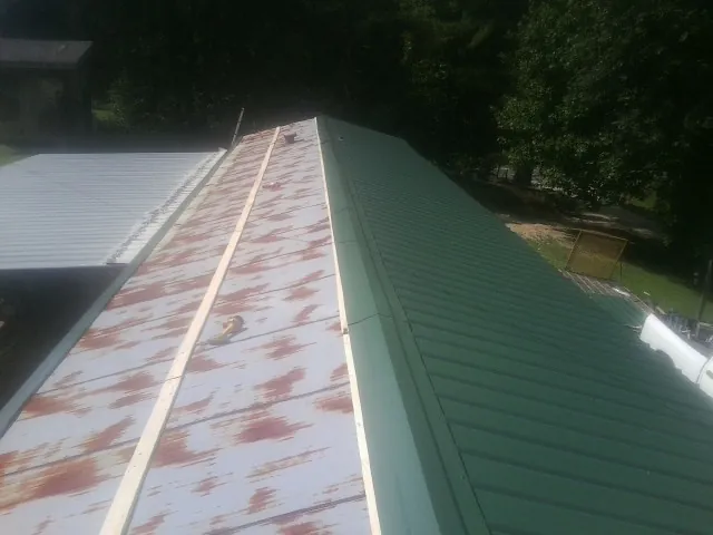 Old rusted panels beside newly installed green metal roofing — Wind Damage Roof Repair by Roofing Brothers in Mesick