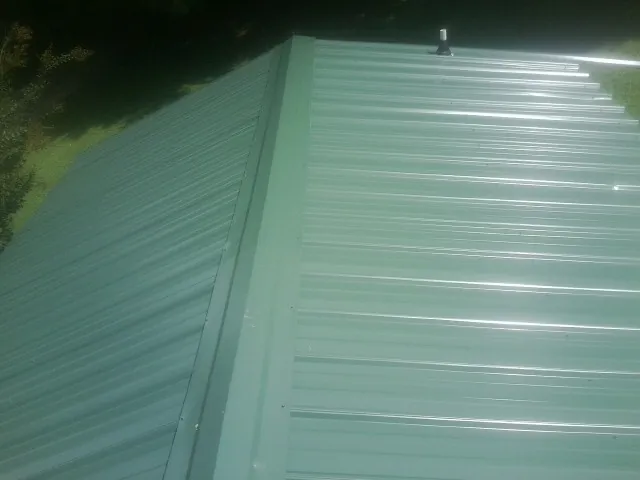 New green metal panels meeting at the ridge of a roof — Flat Roof Repair work by our crew in Mesick