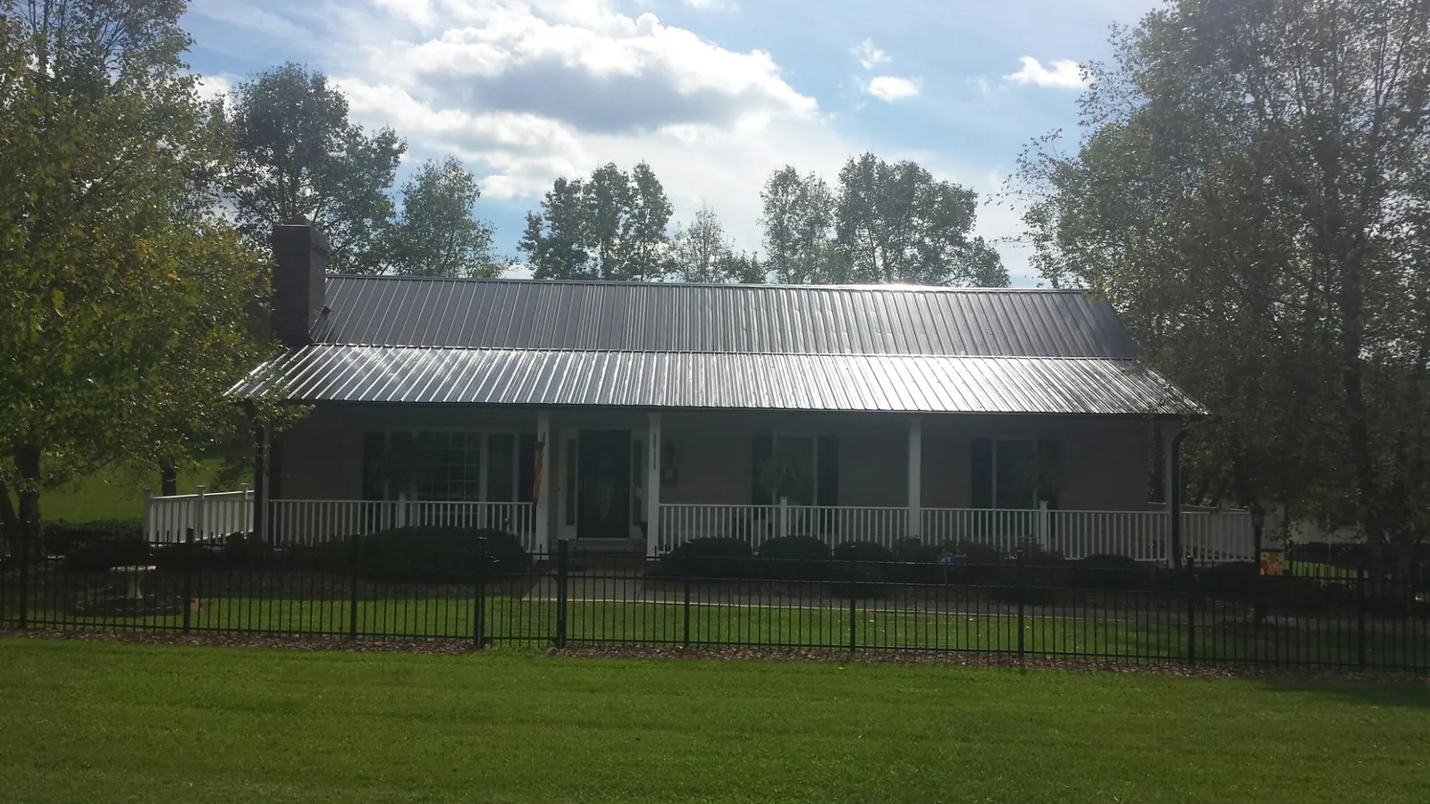 Gray metal roof on a brick ranch with a full width front porch — Gutter Guard Installation work by our crew in Mesick
