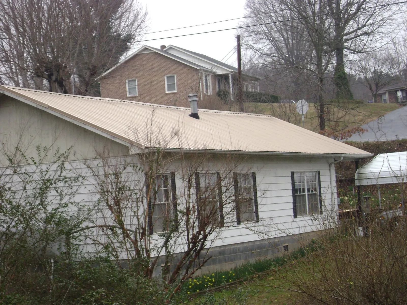 Tan metal roof on a white sided house set into a hillside — Commercial Roofing by Roofing Brothers in Mesick