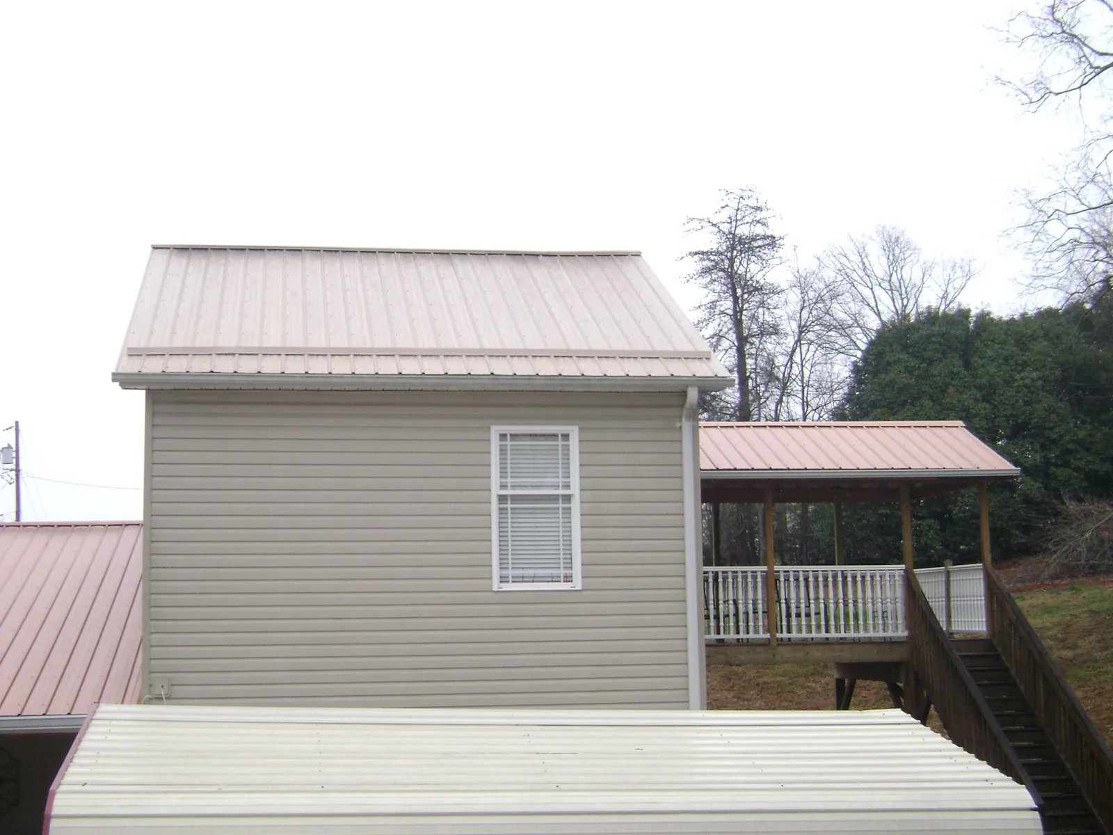 Tan metal roofs on a two story addition and attached porch, from a Roof Replacement job in Mesick